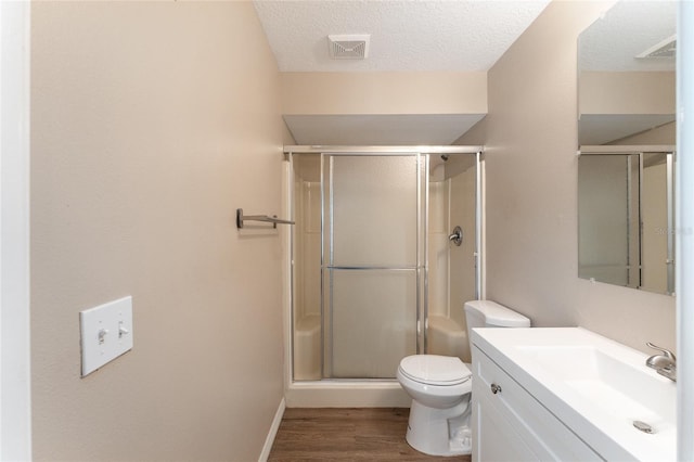 bathroom with wood-type flooring, vanity, toilet, a shower with door, and a textured ceiling