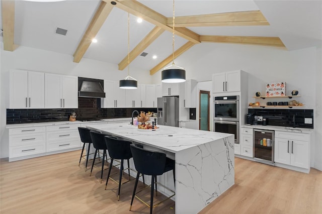 kitchen featuring premium range hood, white cabinetry, hanging light fixtures, stainless steel appliances, and an island with sink