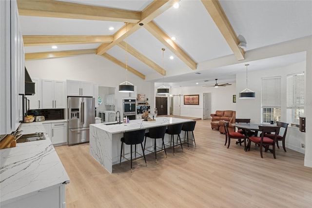 kitchen featuring decorative light fixtures, white cabinetry, a large island with sink, stainless steel appliances, and light stone countertops