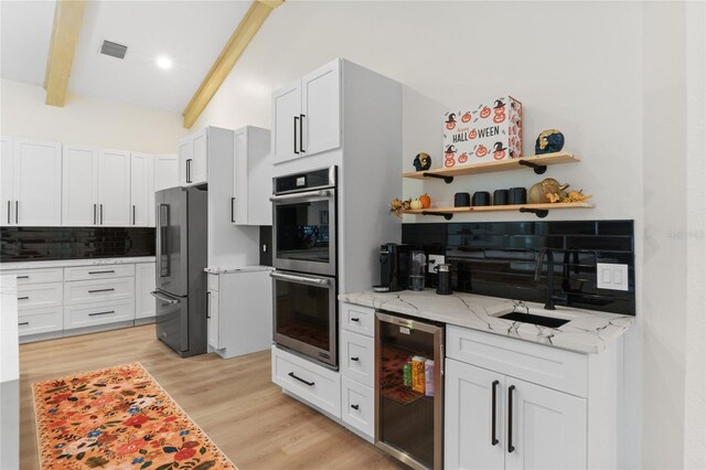 kitchen with stainless steel appliances, white cabinetry, light stone countertops, and sink