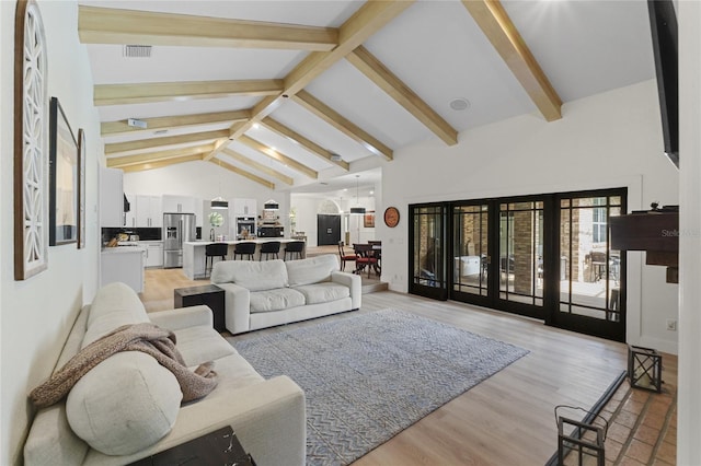 living room featuring high vaulted ceiling, french doors, beamed ceiling, and light wood-type flooring