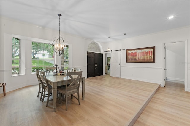 dining space with ornamental molding, a barn door, a notable chandelier, and light hardwood / wood-style floors