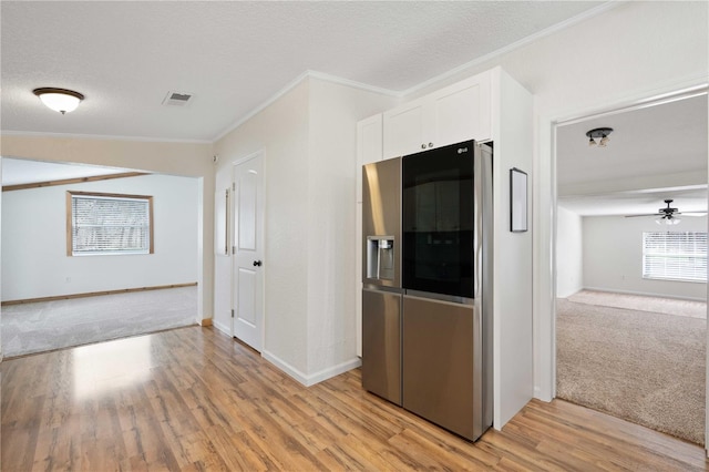 kitchen featuring a textured ceiling, light wood-type flooring, stainless steel refrigerator, ornamental molding, and white cabinets