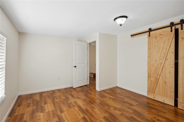 unfurnished bedroom with wood-type flooring and a barn door