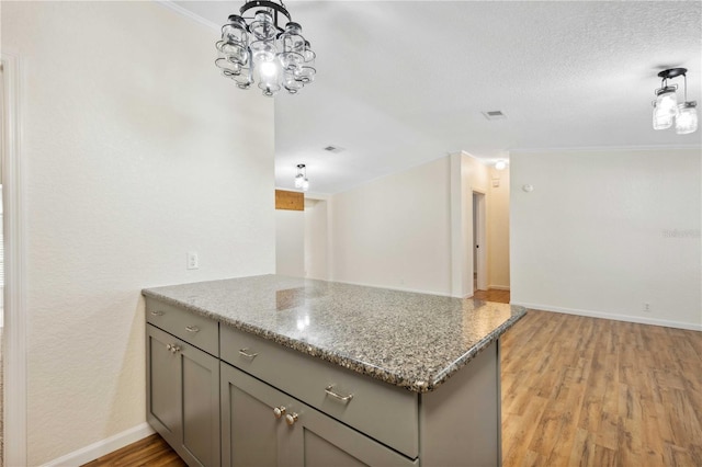 kitchen featuring light hardwood / wood-style flooring, hanging light fixtures, light stone countertops, a textured ceiling, and kitchen peninsula