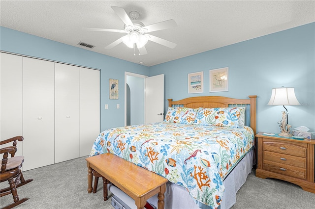 bedroom featuring ceiling fan, light colored carpet, a textured ceiling, and a closet