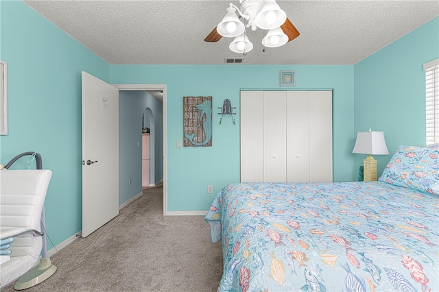 bedroom featuring ceiling fan, a closet, light carpet, and a textured ceiling