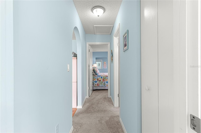 hallway with light colored carpet and a textured ceiling