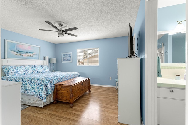 bedroom with ceiling fan, ensuite bath, light hardwood / wood-style flooring, and a textured ceiling