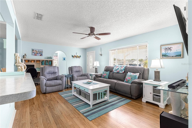 living room with ceiling fan, light hardwood / wood-style flooring, and a textured ceiling