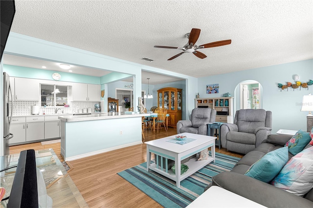 living room with ceiling fan, light hardwood / wood-style flooring, and a textured ceiling