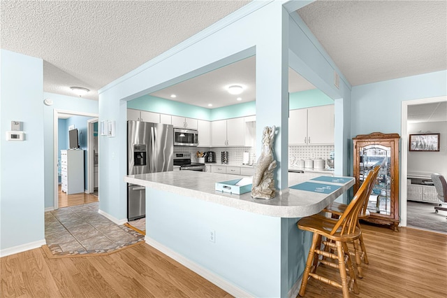 kitchen featuring white cabinetry, light hardwood / wood-style flooring, stainless steel appliances, and tasteful backsplash