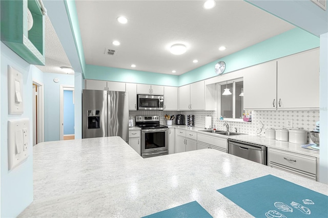 kitchen featuring sink, appliances with stainless steel finishes, backsplash, white cabinets, and kitchen peninsula