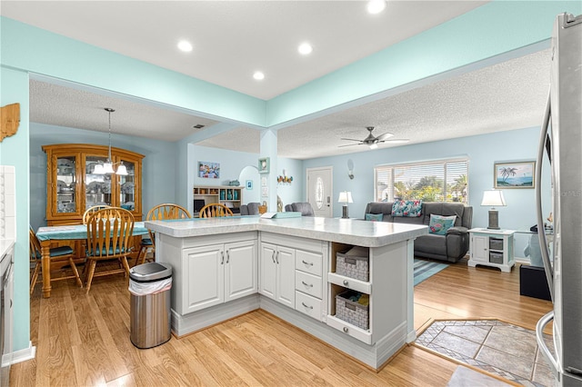 kitchen with light hardwood / wood-style flooring, kitchen peninsula, hanging light fixtures, and white cabinets