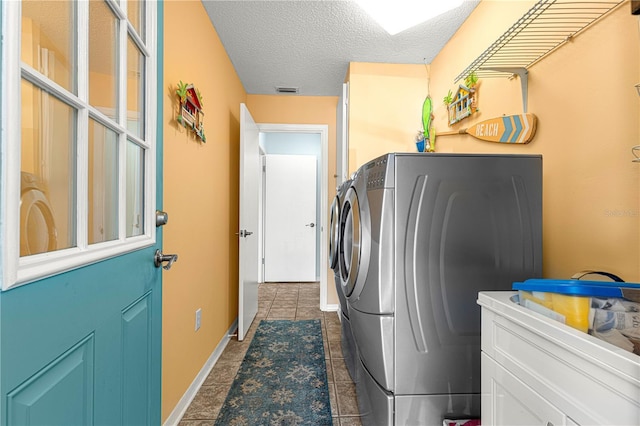 laundry room featuring washing machine and clothes dryer, dark tile patterned floors, and a textured ceiling