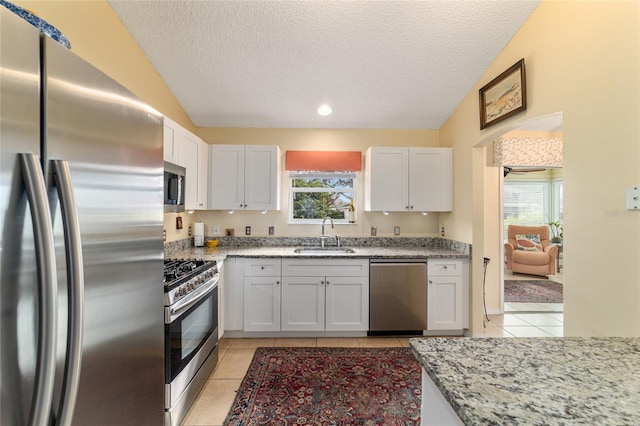 kitchen with lofted ceiling, sink, white cabinetry, stainless steel appliances, and light stone countertops