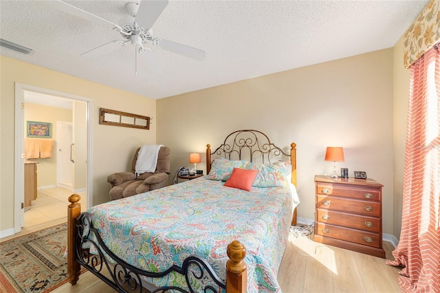 bedroom featuring ceiling fan, ensuite bath, light hardwood / wood-style floors, and a textured ceiling