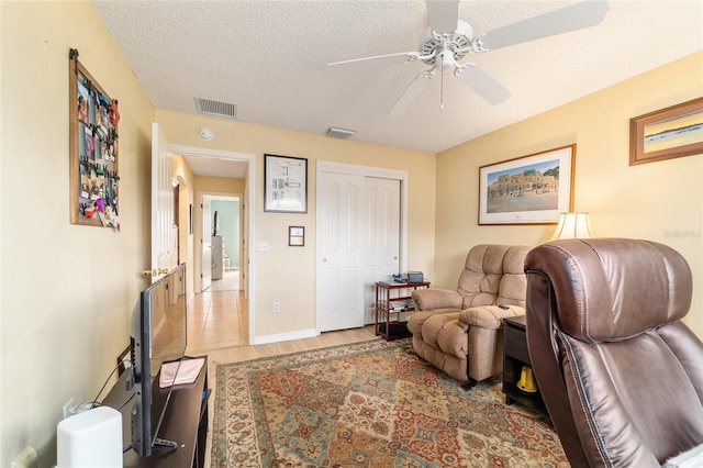 living room with ceiling fan, light hardwood / wood-style flooring, and a textured ceiling