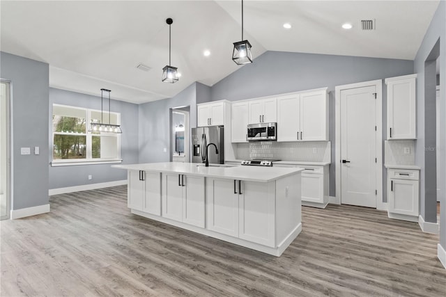 kitchen with hanging light fixtures, an island with sink, stainless steel appliances, light hardwood / wood-style floors, and white cabinets