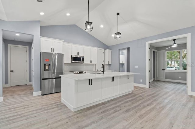 kitchen featuring decorative light fixtures, sink, white cabinets, stainless steel appliances, and a center island with sink