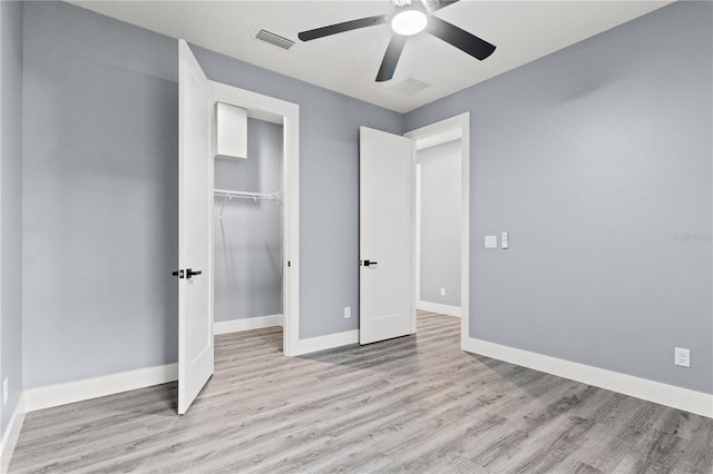 unfurnished bedroom featuring ceiling fan, a closet, light hardwood / wood-style flooring, and a walk in closet