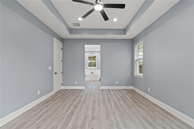 empty room featuring a tray ceiling, ceiling fan, and light wood-type flooring