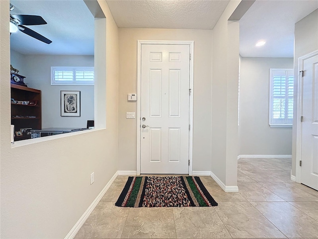 foyer entrance with ceiling fan and a textured ceiling