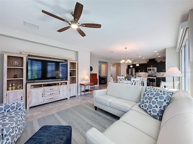 tiled living room with ceiling fan with notable chandelier and a textured ceiling