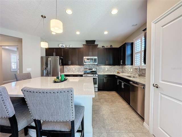 kitchen featuring hanging light fixtures, a kitchen island, sink, tasteful backsplash, and appliances with stainless steel finishes