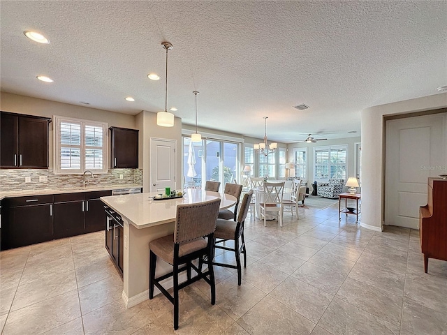 kitchen with hanging light fixtures, a center island, dark brown cabinetry, backsplash, and a breakfast bar area