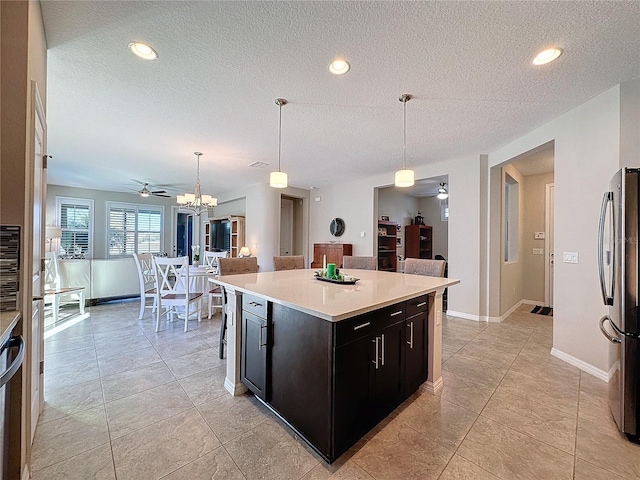 kitchen featuring a textured ceiling, pendant lighting, stainless steel refrigerator, a center island, and ceiling fan with notable chandelier