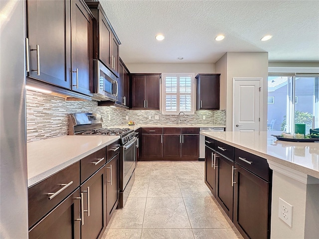 kitchen with appliances with stainless steel finishes, sink, a textured ceiling, dark brown cabinets, and tasteful backsplash