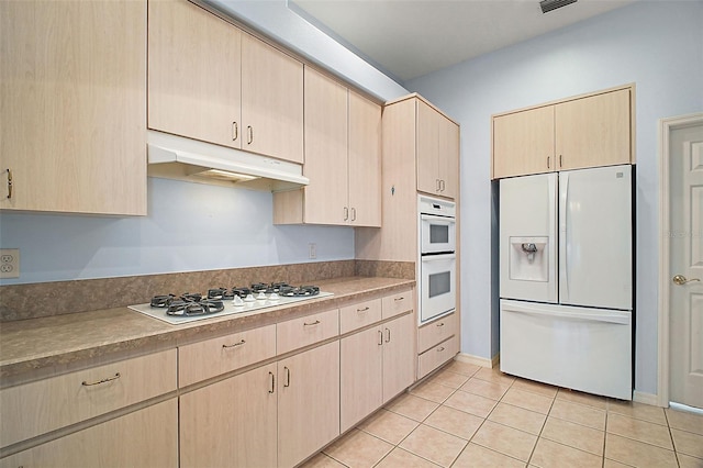 kitchen featuring light tile patterned floors, light brown cabinetry, and white appliances