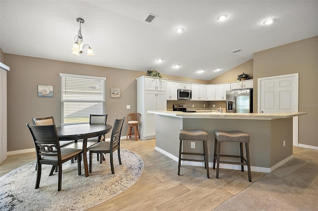 kitchen featuring white cabinetry, hanging light fixtures, a kitchen breakfast bar, an island with sink, and stainless steel appliances