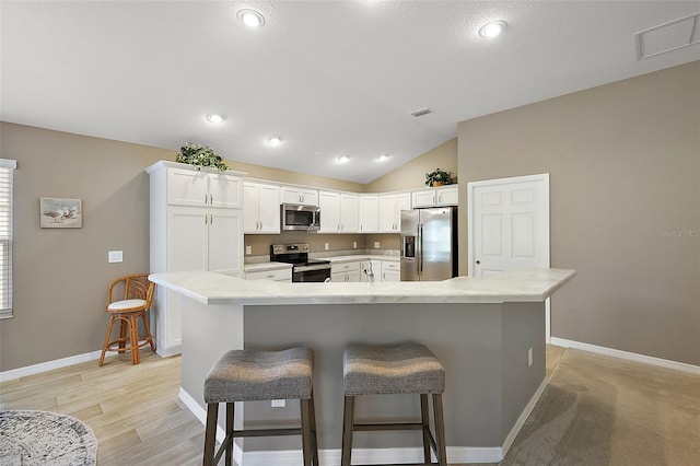 kitchen with vaulted ceiling, appliances with stainless steel finishes, a breakfast bar area, white cabinets, and a center island