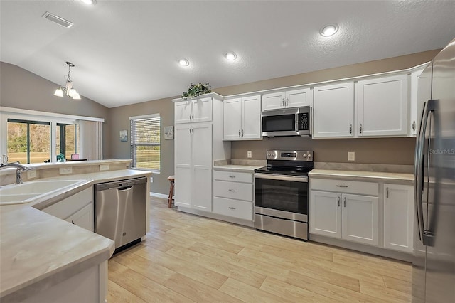 kitchen with sink, light hardwood / wood-style flooring, appliances with stainless steel finishes, hanging light fixtures, and white cabinets