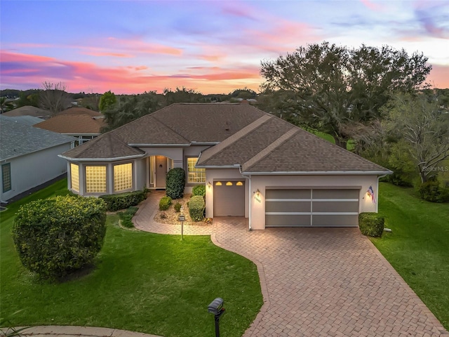 ranch-style home with decorative driveway, a yard, stucco siding, a shingled roof, and an attached garage