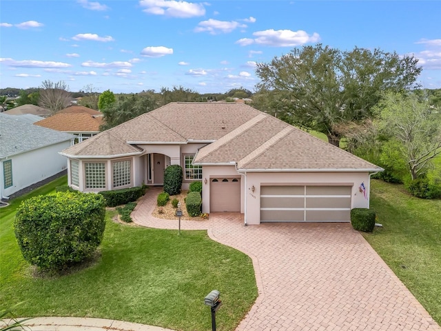 single story home with roof with shingles, an attached garage, decorative driveway, a front lawn, and stucco siding