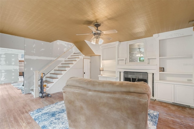 living room featuring ceiling fan, light hardwood / wood-style floors, a tile fireplace, and built in features