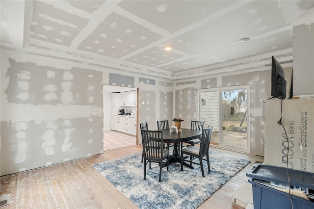 dining area with coffered ceiling and light hardwood / wood-style floors