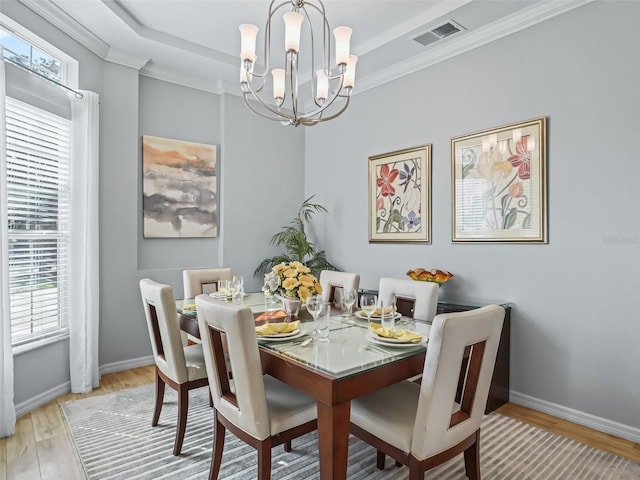 dining space featuring a tray ceiling, ornamental molding, light hardwood / wood-style floors, and a chandelier