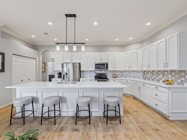 kitchen with a kitchen bar, a center island with sink, pendant lighting, stainless steel appliances, and white cabinets