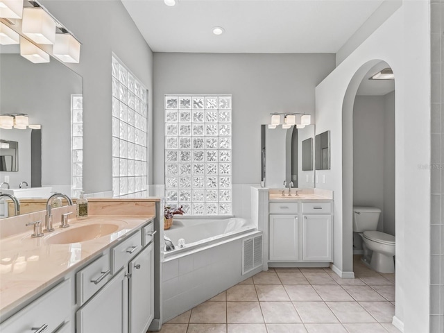 bathroom with vanity, tile patterned flooring, tiled bath, and toilet