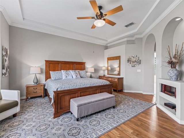 bedroom featuring ceiling fan, ornamental molding, a tray ceiling, and light hardwood / wood-style floors