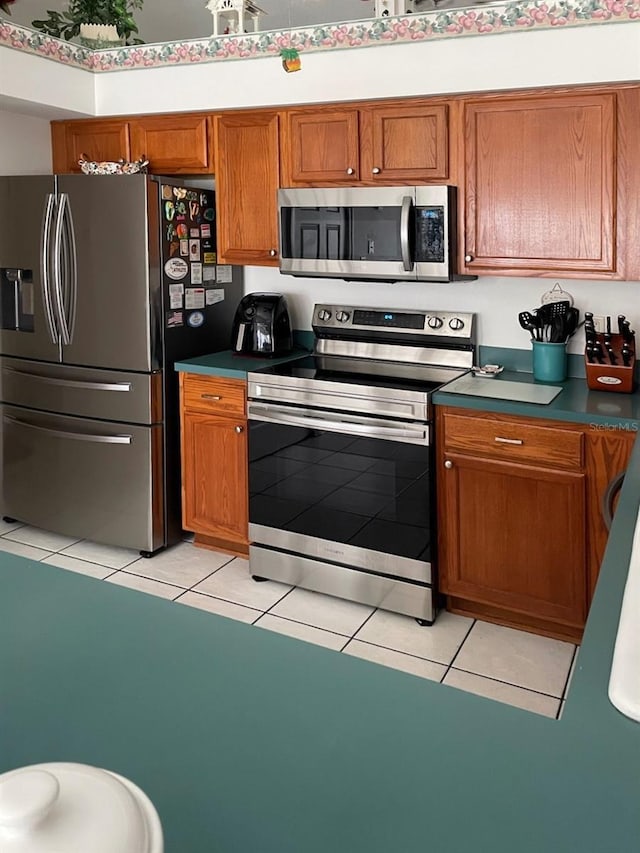 kitchen with light tile patterned flooring, dark countertops, stainless steel appliances, and brown cabinetry