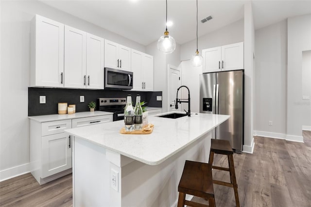 kitchen featuring visible vents, a kitchen bar, a sink, white cabinetry, and appliances with stainless steel finishes