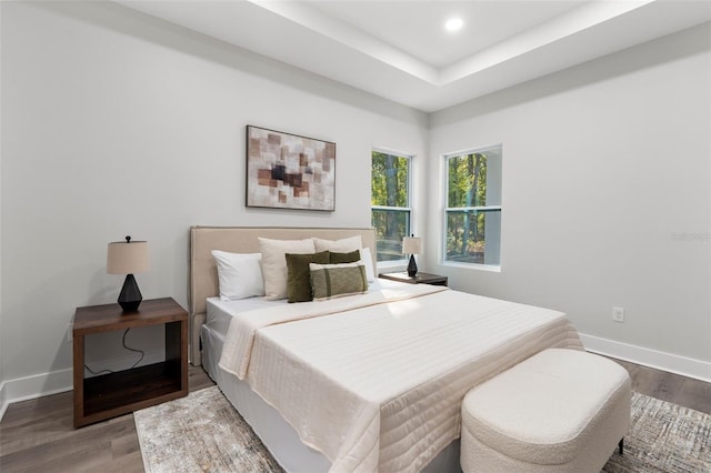 bedroom with recessed lighting, a tray ceiling, baseboards, and wood finished floors