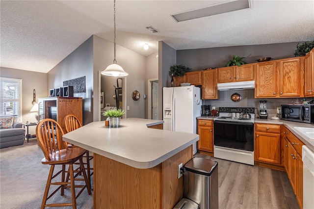 kitchen with white appliances, vaulted ceiling, decorative light fixtures, and a kitchen bar