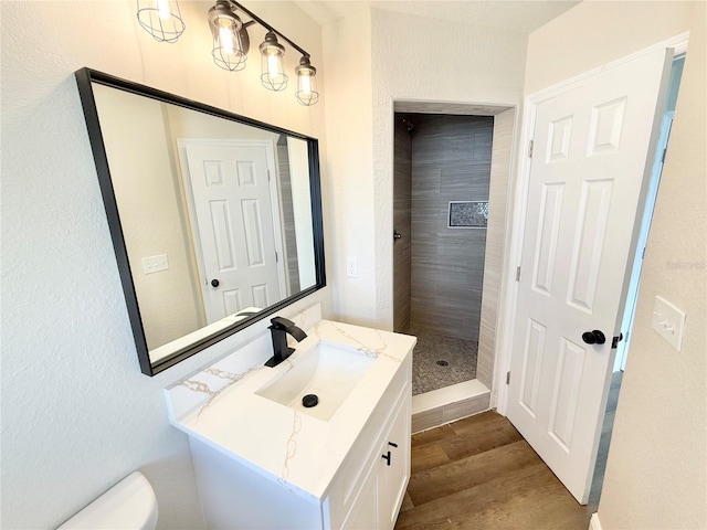 bathroom with vanity, tiled shower, hardwood / wood-style floors, and toilet