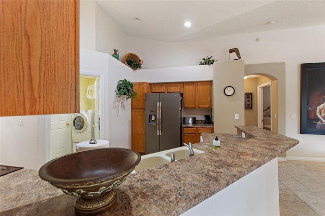 kitchen with washer / dryer, vaulted ceiling, stainless steel fridge with ice dispenser, light tile patterned floors, and light stone countertops